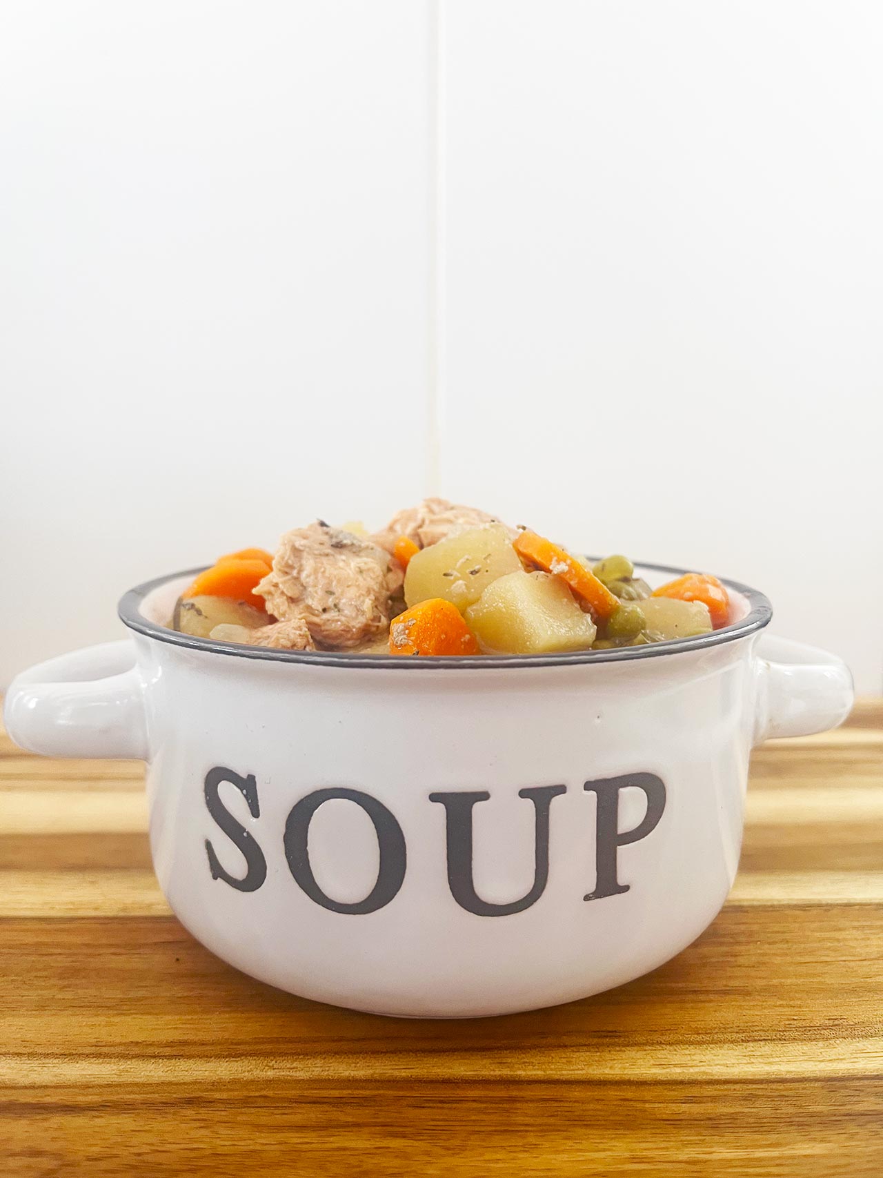 Eye level focus. A white crock filled with Slow Cooker chicken Cobbler Stew.