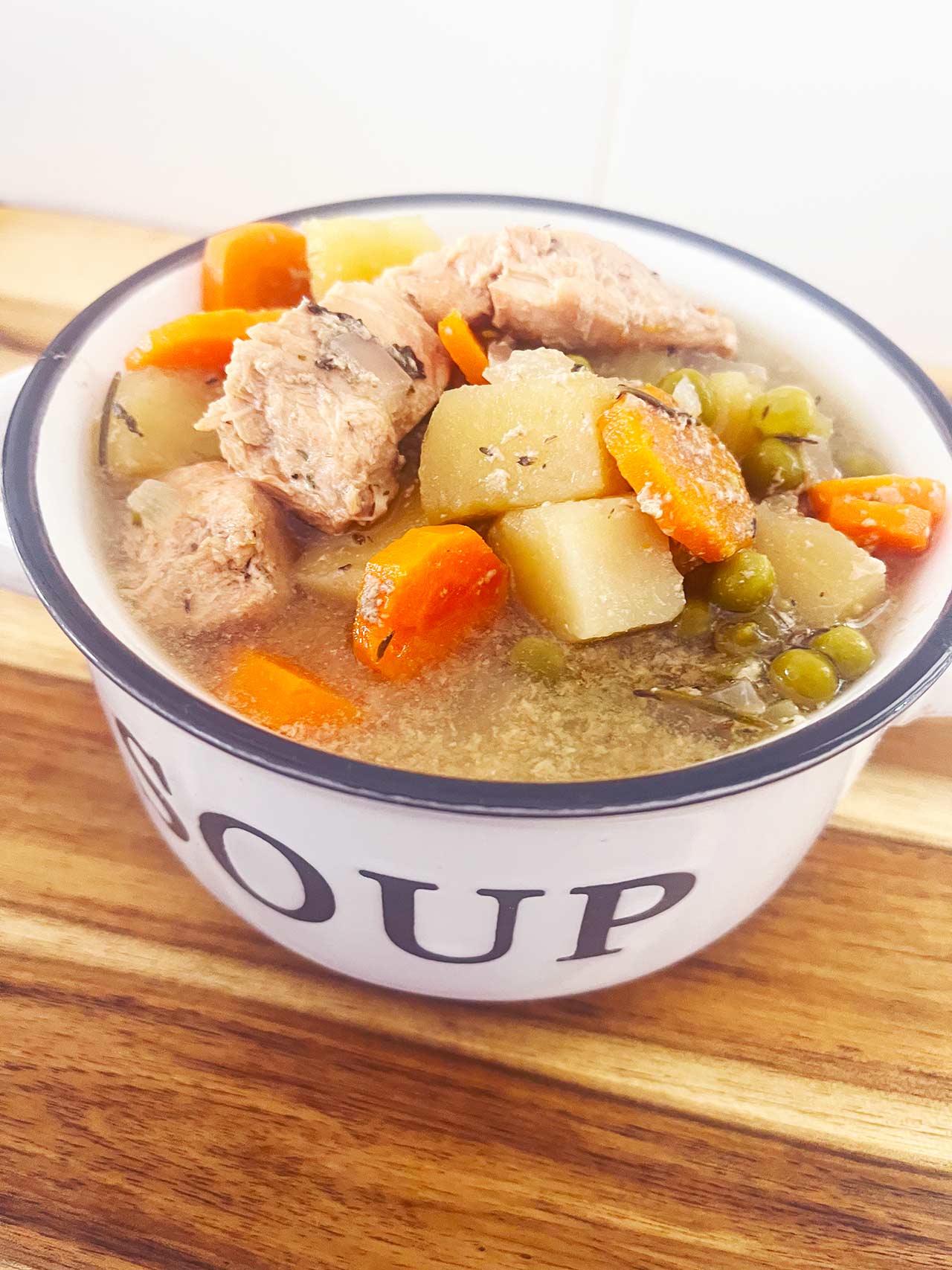 Angled overhead focus. A white crock filled with Slow Cooker chicken Cobbler Stew.