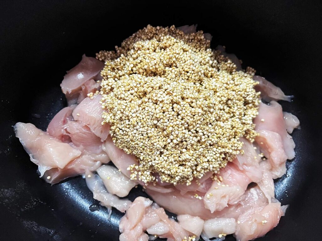 Rinsed quinoa added to chicken in a slow cooker crock.