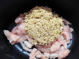 Rinsed quinoa added to chicken in a slow cooker crock.