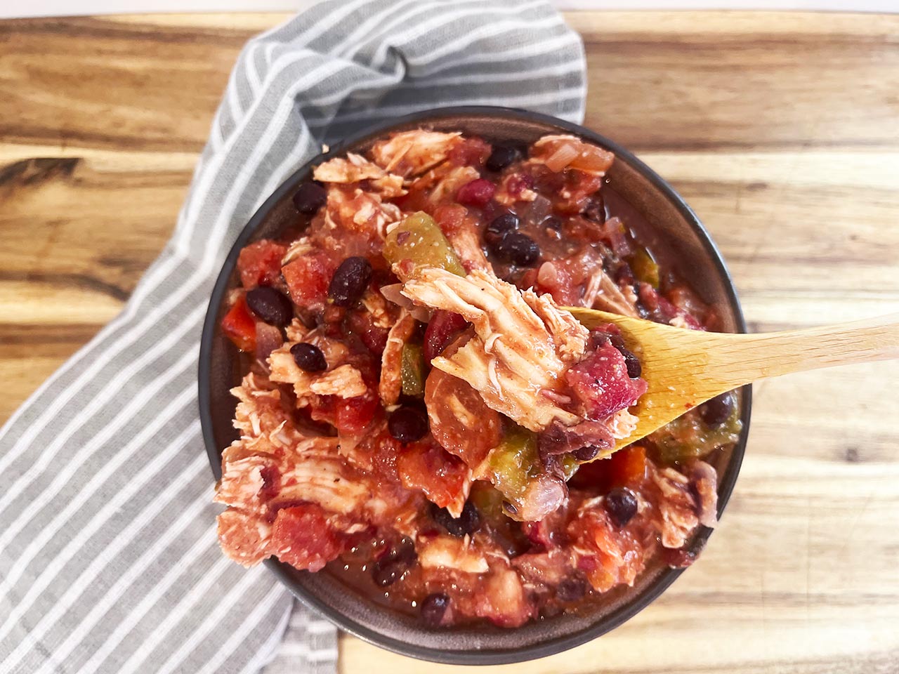 Overhead focus. A wood spoon lifts up a bite of Slow Cooker Chicken Taco Stew from a bowl.