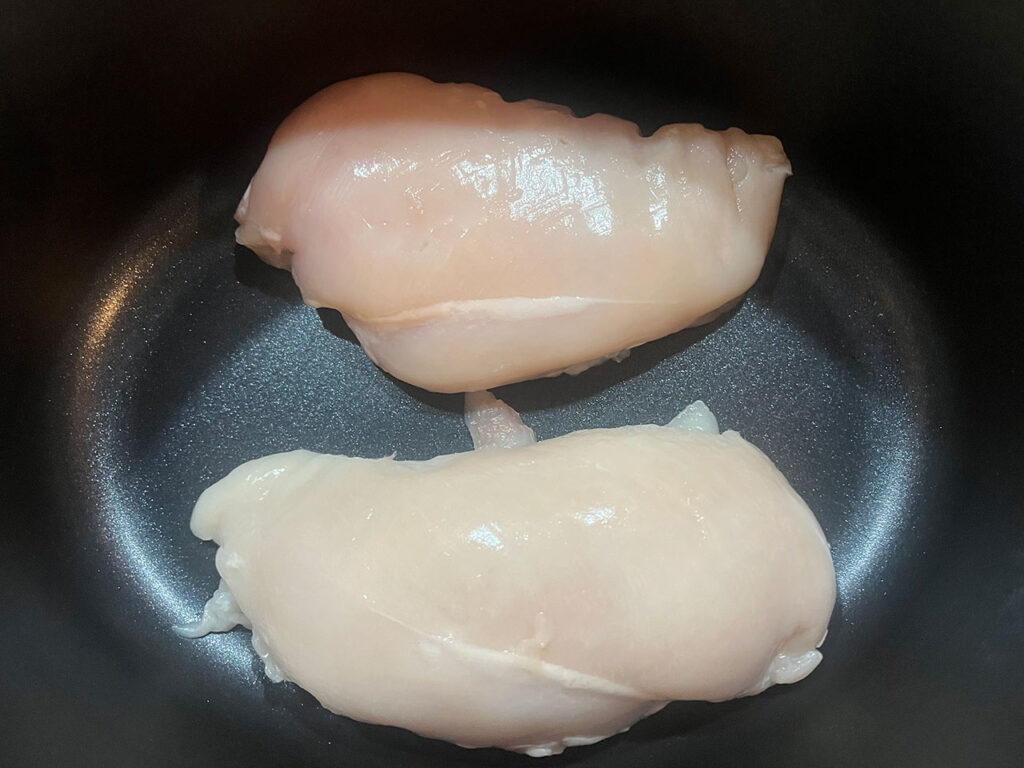 Two chicken breasts in a slow cooker crock.