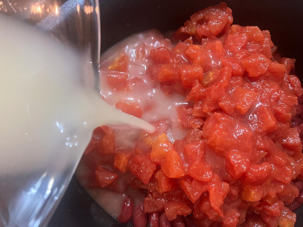 Diced tomatoes and chicken broth added to a slow cooker crock.