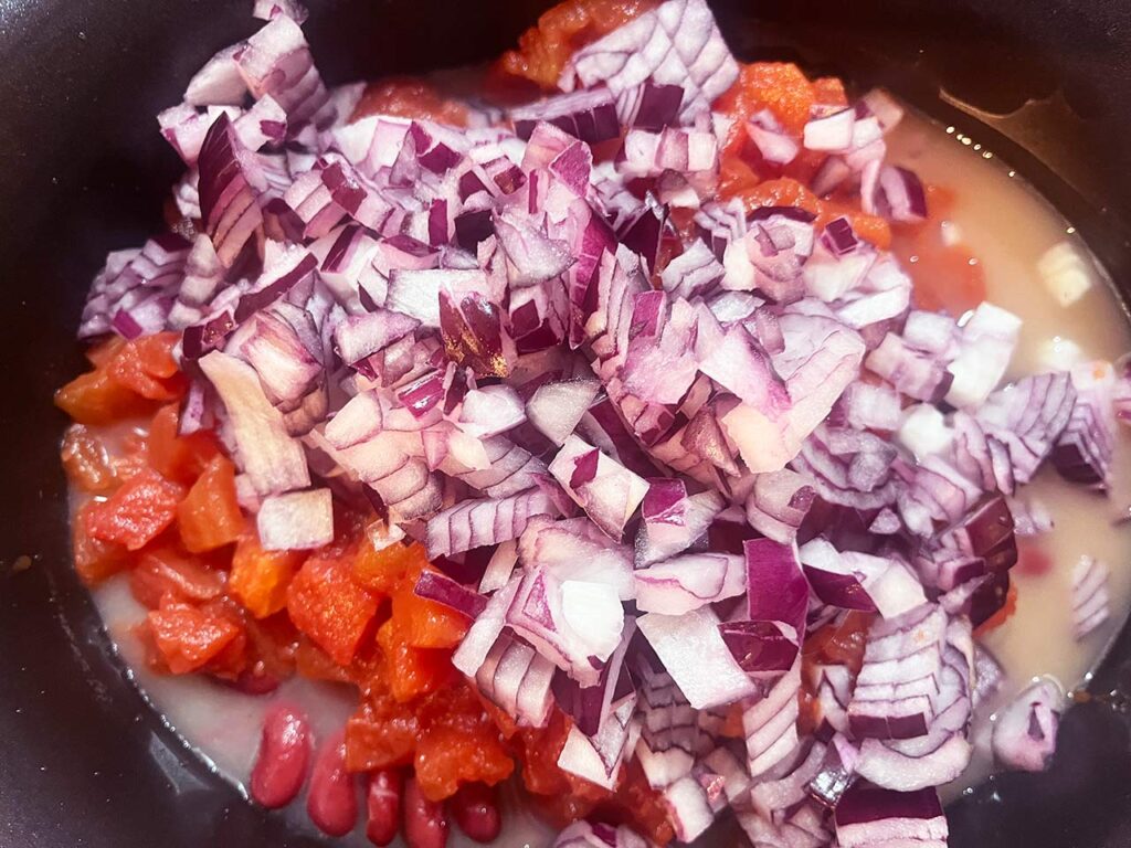 Chopped, red onions added to other ingredients in a slow cooker crock.