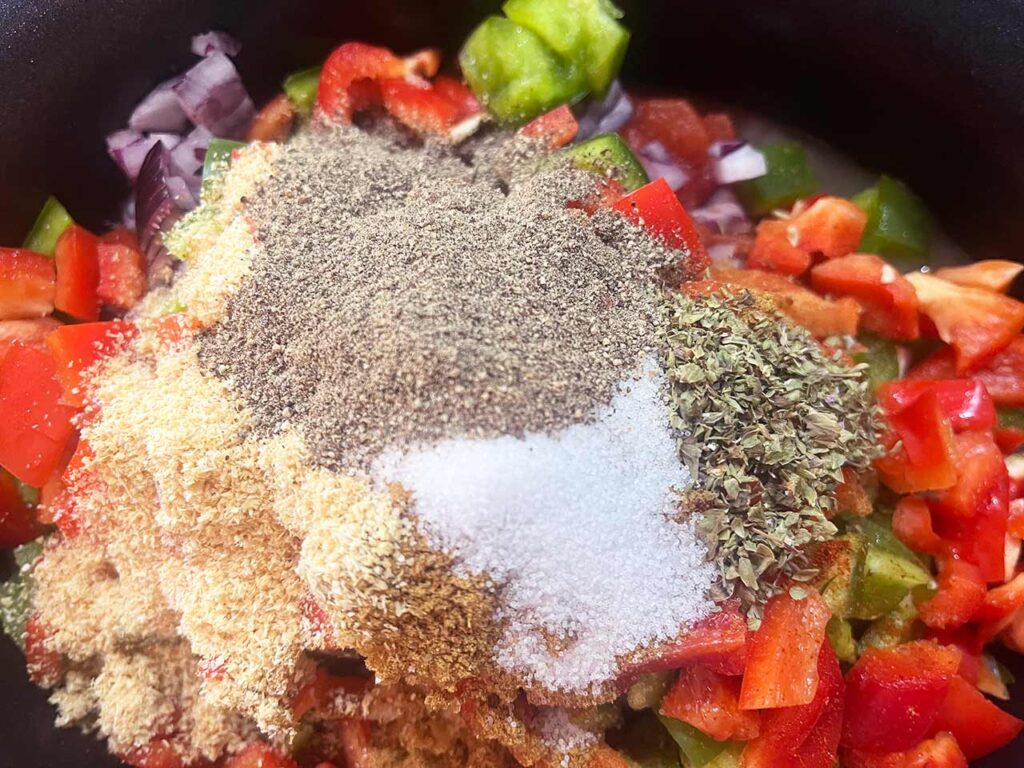 Dried herbs, spices, salt and pepper added to ingredients in a slow cooker crock.