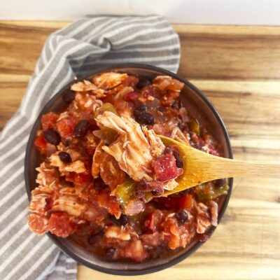 Overhead focus. A bowl filled with Slow Cooker Chicken Taco Stew. A wood spoon lifts up a bite.