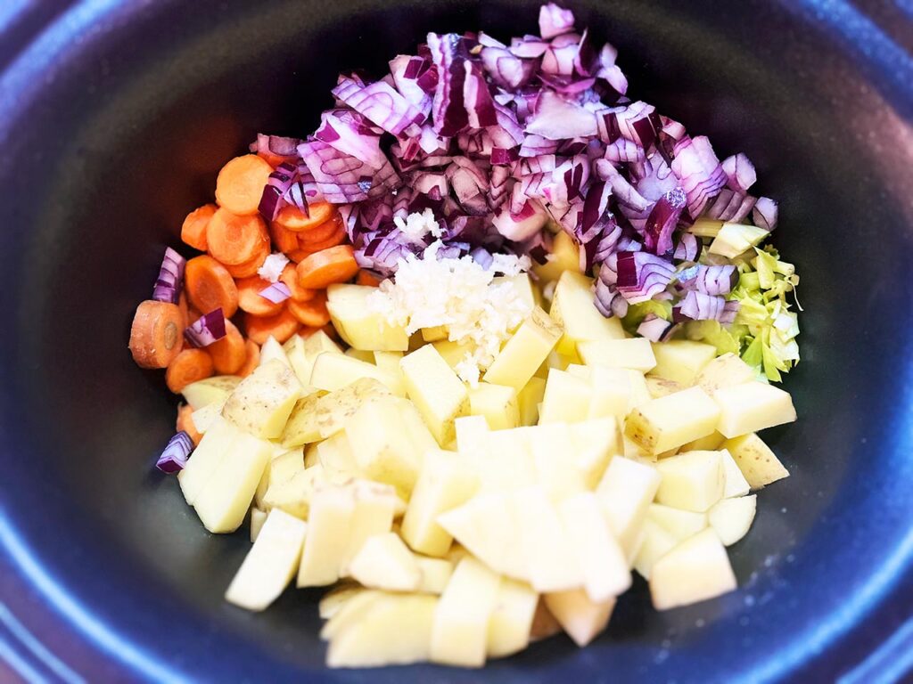 Potatoes, carrots, celery, onions, and pressed garlic in a slow cooker crock.