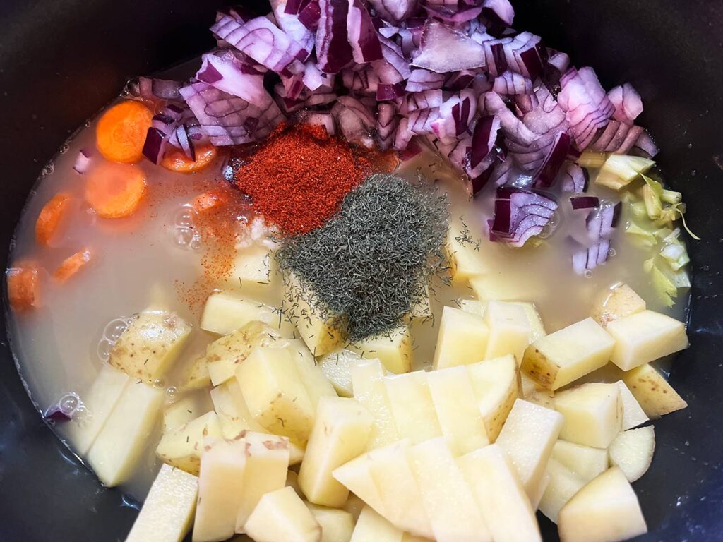 Stock and spices added to veggies in a slow cooker crock.