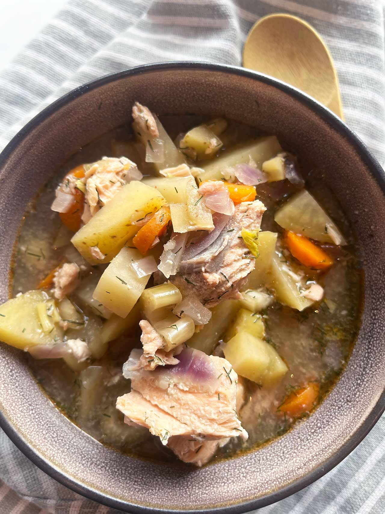 Overhead focus closeup. A bowl of Slow Cooker Salmon Stew With Potatoes on a striped towel.