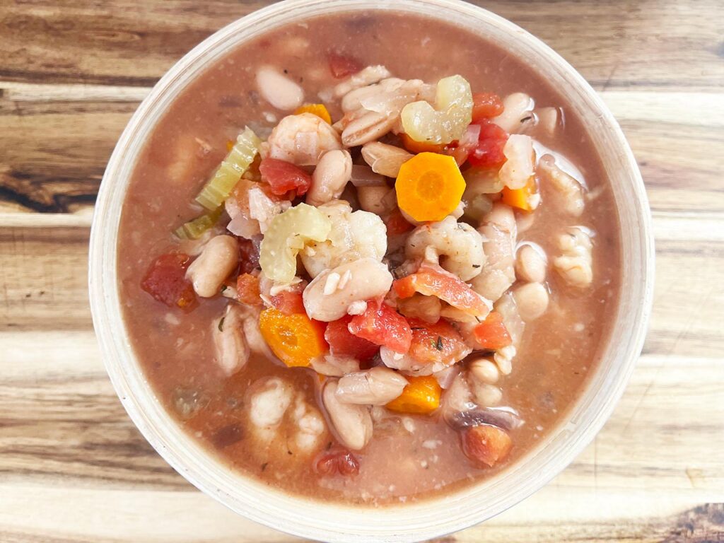 Overhead focus. A full bowl of Slow Cooker Shrimp And White Bean Stew on a wood surface.