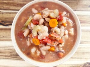 Overhead focus. A full bowl of Slow Cooker Shrimp And White Bean Stew on a wood surface.