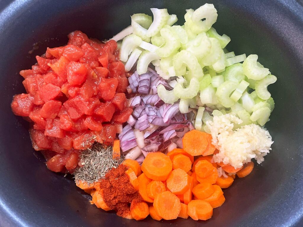 Slow Cooker Shrimp And White Bean Stew Recipe ingredients in a slow cooker crock. Chopped veggies and spices.