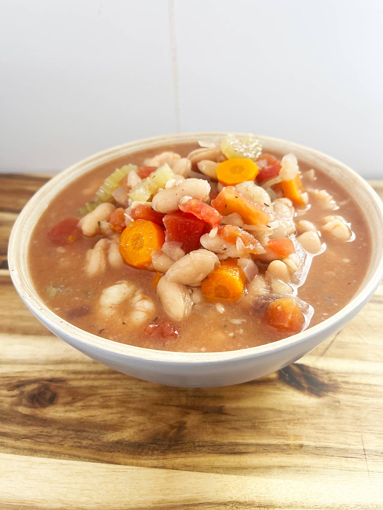 Front angled focus. A full bowl of Slow Cooker Shrimp And White Bean Stew sitting on a wood surface.