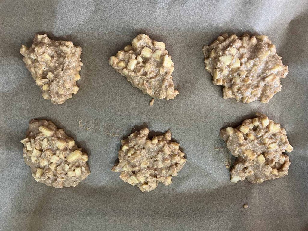 Apple cookie batter spooned onto a parchment-lined baking sheet.
