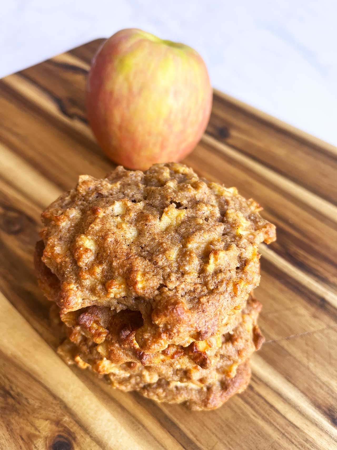 Angled overhead focus of four apple cookies in a stack. An apple sits behind the stack.