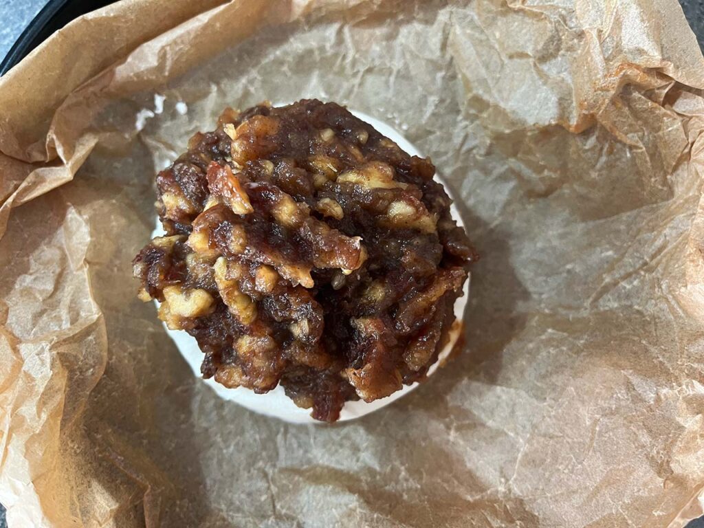 Date and walnut paste added to the top of a brie round in a parchment-lined dish.