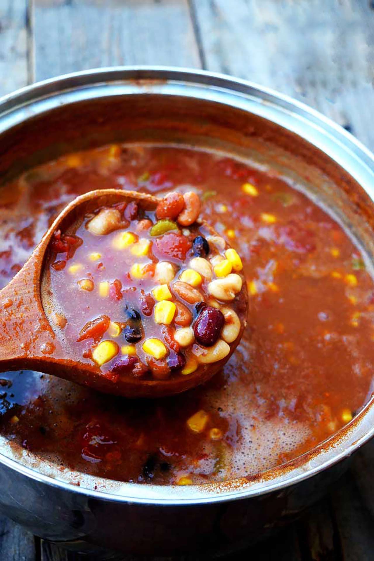 A wood ladle scoops up a ladle full of Bean Chowder from a large pot.