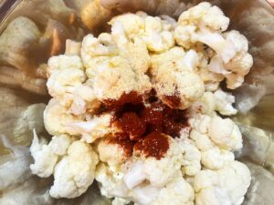 Spices added to cauliflower florets and oil in a mixing bowl.