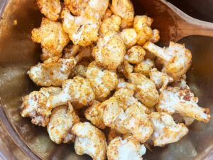 Cauliflower florets mixed with spices and oil in a mixing bowl.