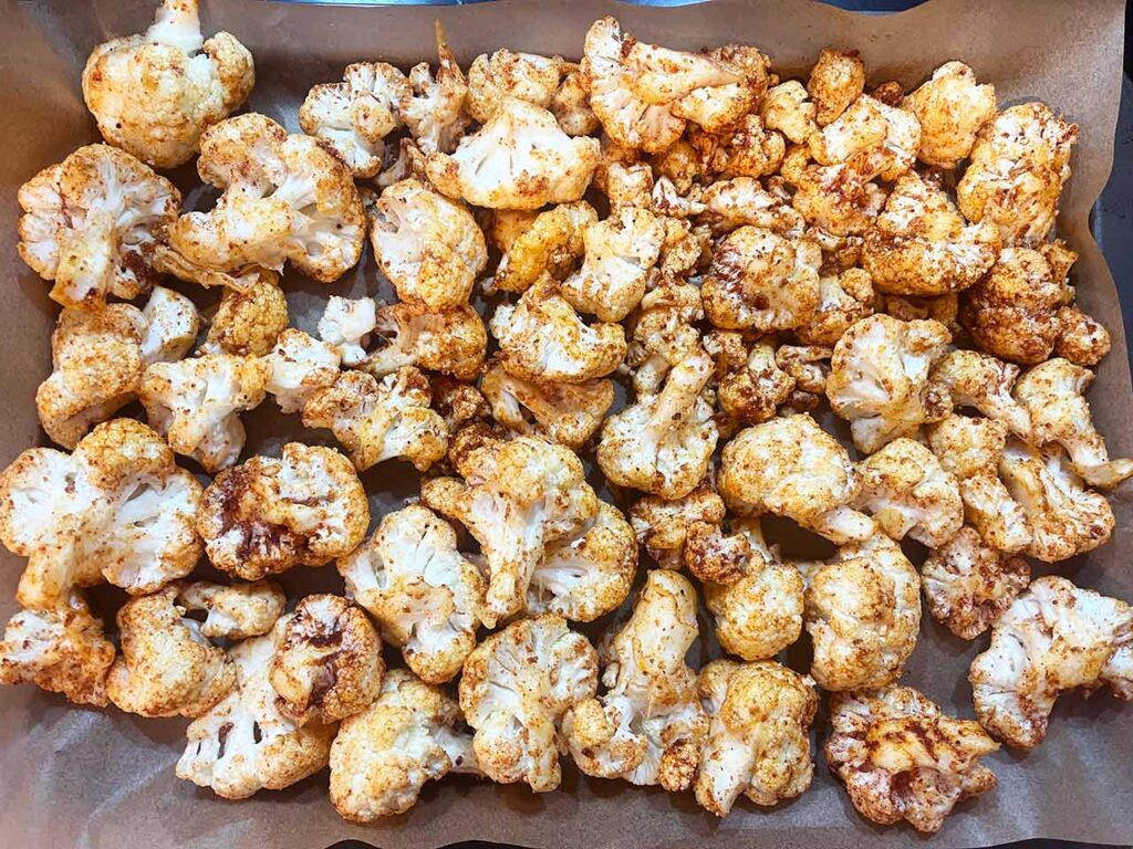 Seasoned cauliflower florets spread out over a parchment-lined baking sheet.