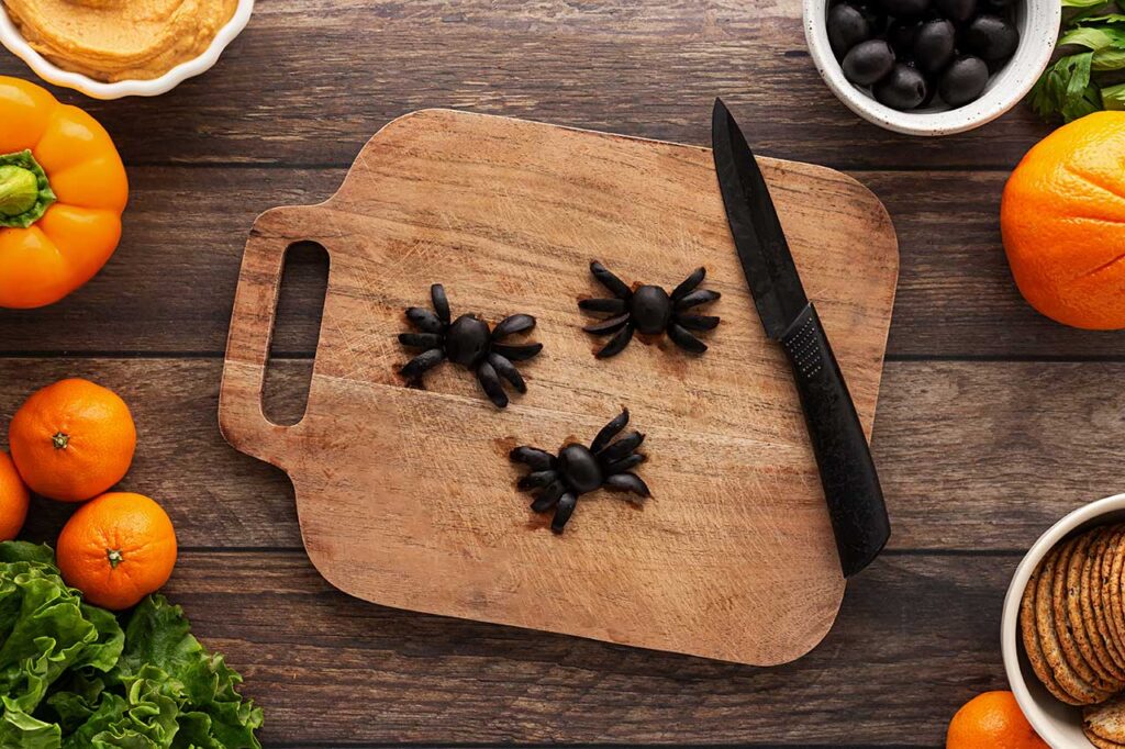 Olives formed into the shape of spiders on a cutting board.