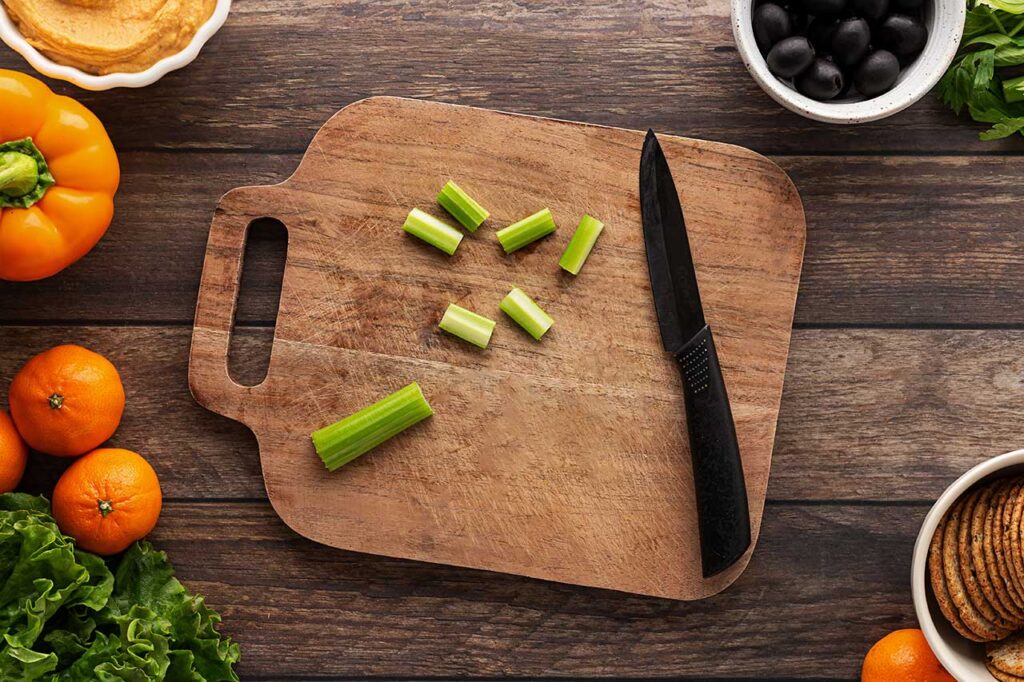 Celery cut into small pumpkin stems on a cutting board.