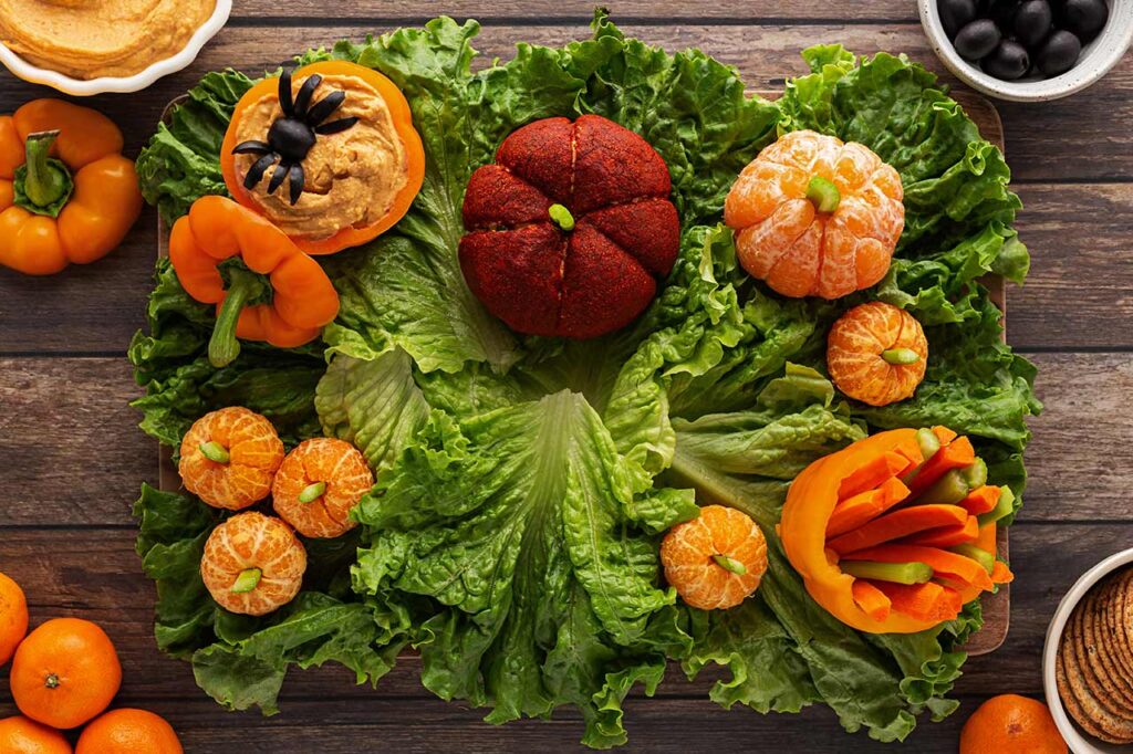 A hollowed out, orange bell pepper filled with carrot and celery stick placed on the lower right corner of the board.