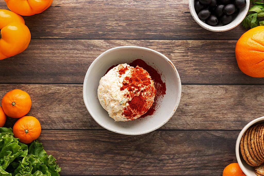 A cheese ball partially rolled in ground paprika. Overhead focus.