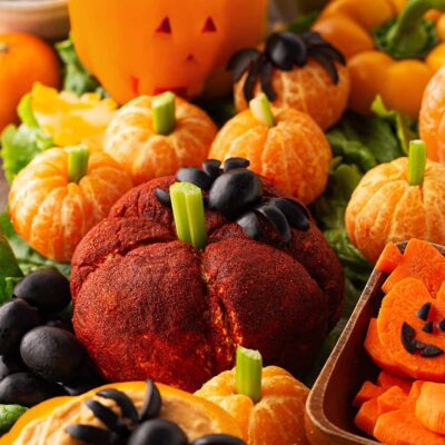 A cheese ball colored with paprika and shaped into a pumpkin with a celery stem.
