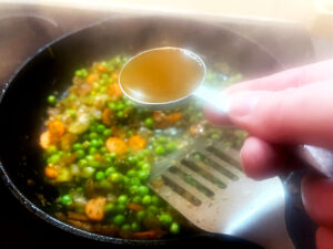Adding apple cider vinegar to the veggies in a skillet.