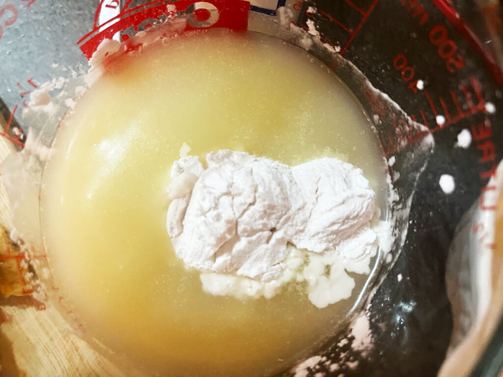 Arrowroot powder added to chicken broth in a measuring cup.