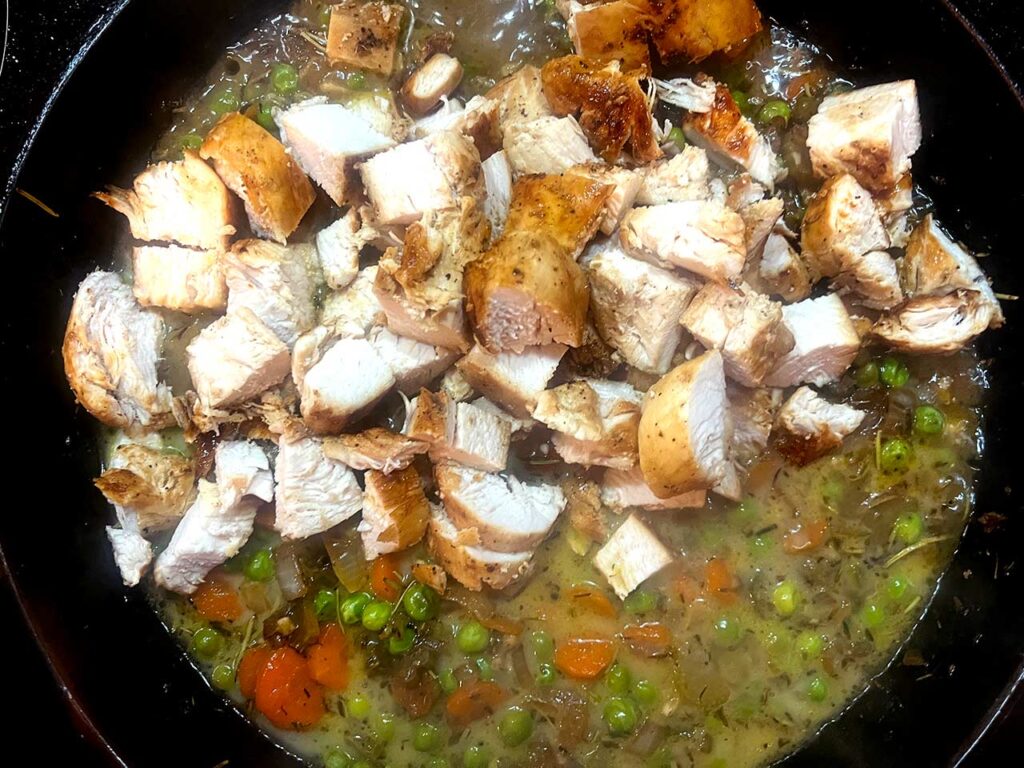 Chicken chunks added to veggies and broth in a skillet.