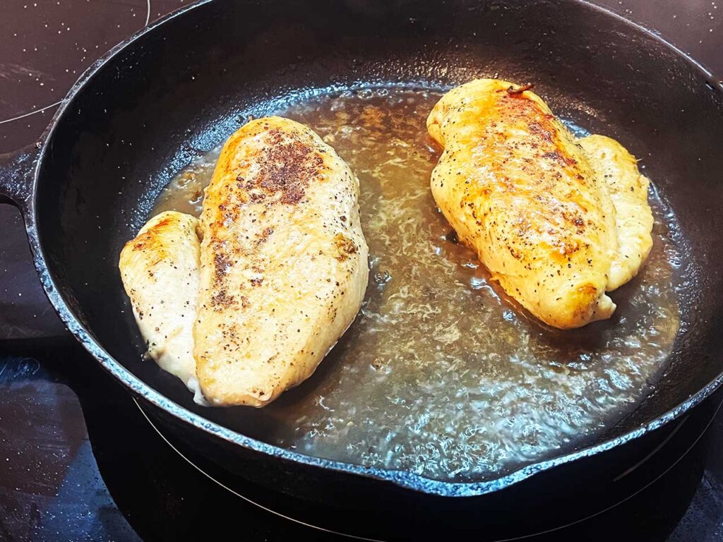 Two cooked chicken breasts in a skillet.