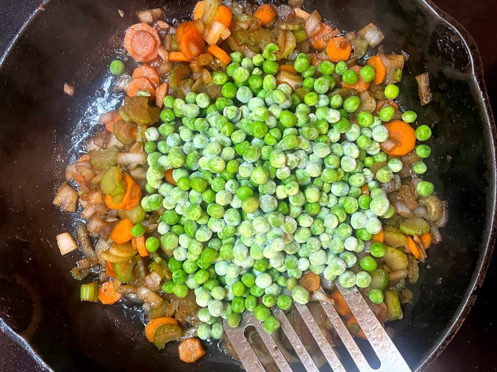 Frozen peas added to veggies in a skillet.