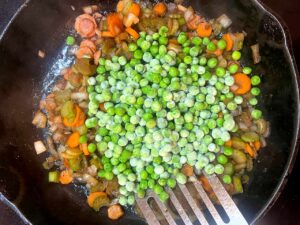 Frozen peas added to veggies in a skillet.