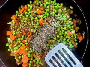 Dried herbs added to veggies in a skillet.