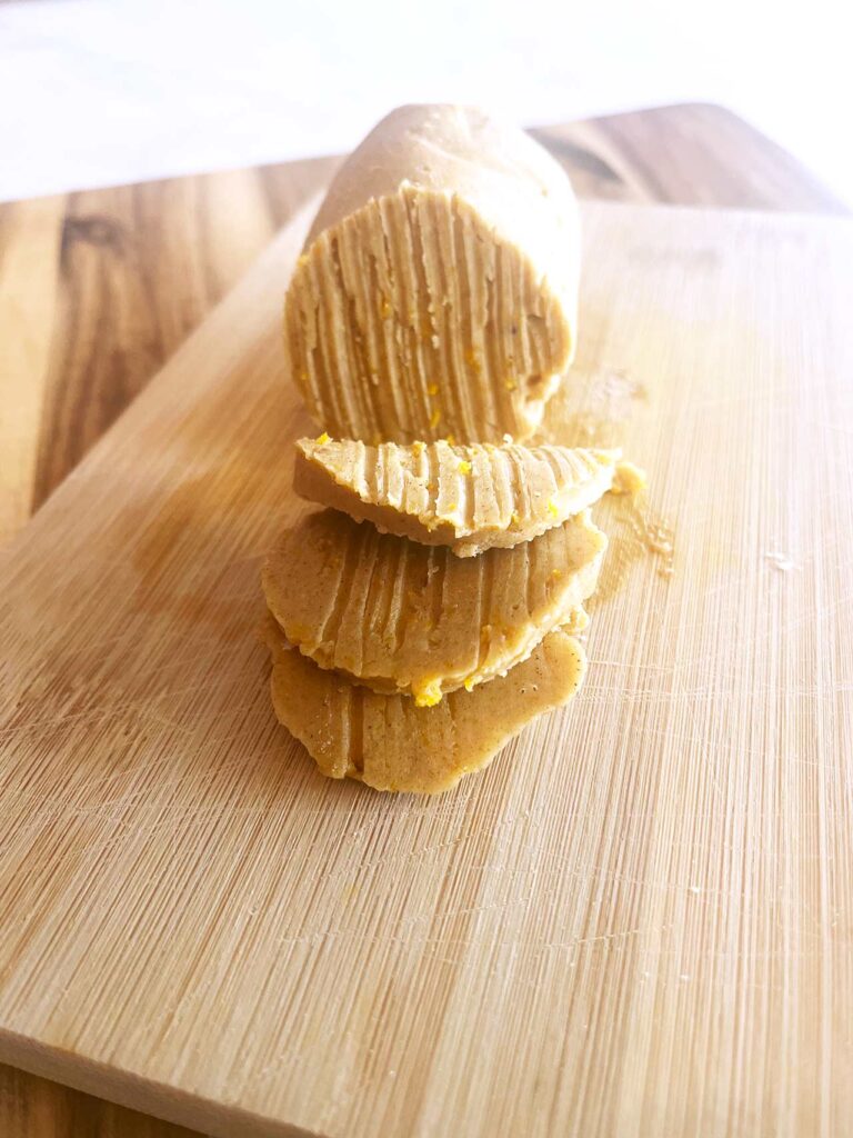 Front focus. A wood cutting board with a log of compound butter on it. Three slices of butter lay in front of the log.