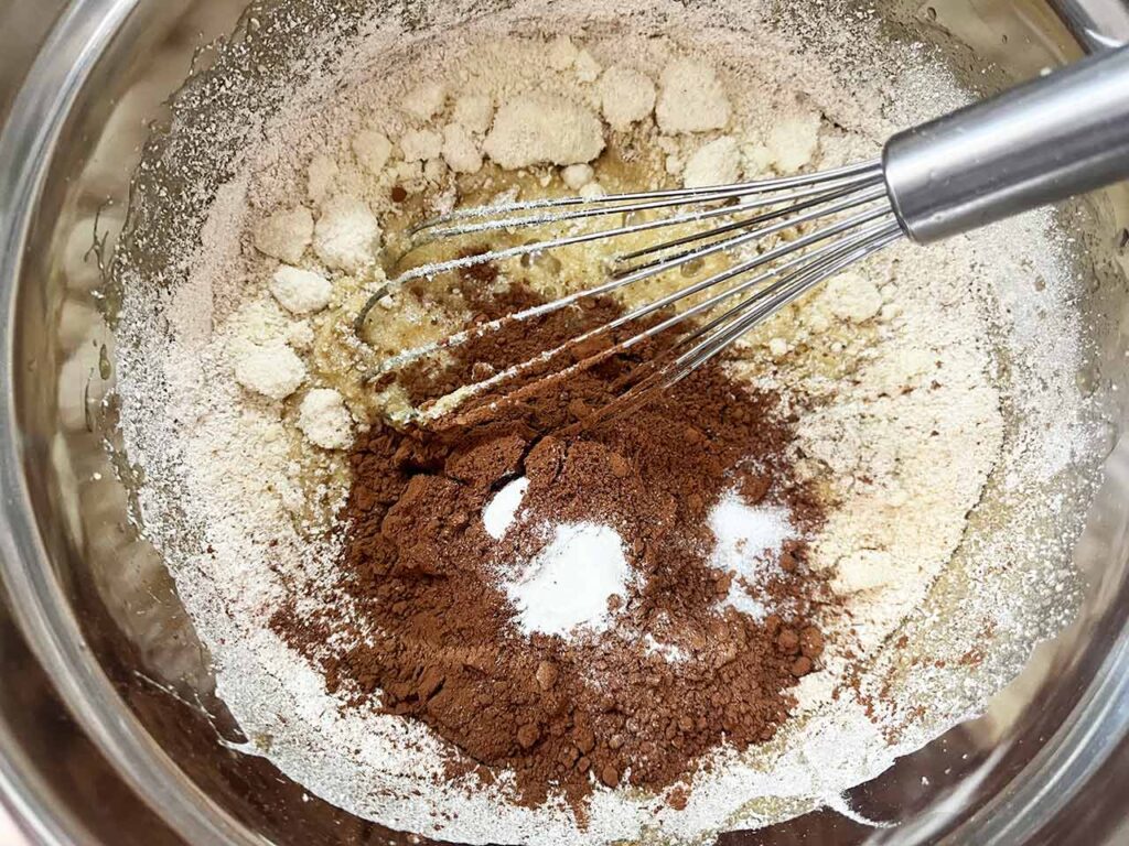 Dry ingredients for cream cheese brownies added to wet ingredients in a metal mixing bowl.