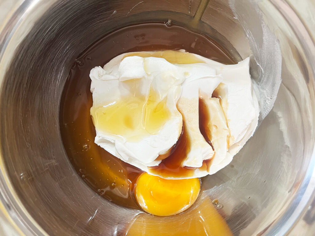 Egg, honey, and vanilla extract added to cream cheese in a metal mixing bowl.
