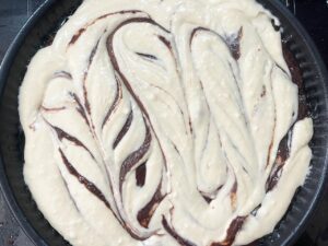 Swirled cream cheese in brownie batter in a baking pan.