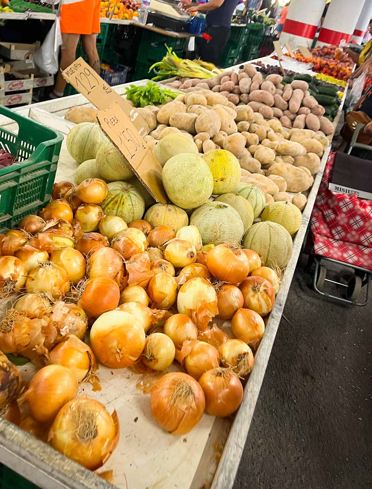 A table of onions, melons, and potatoes for sale at the open market in El Campello, Spain.