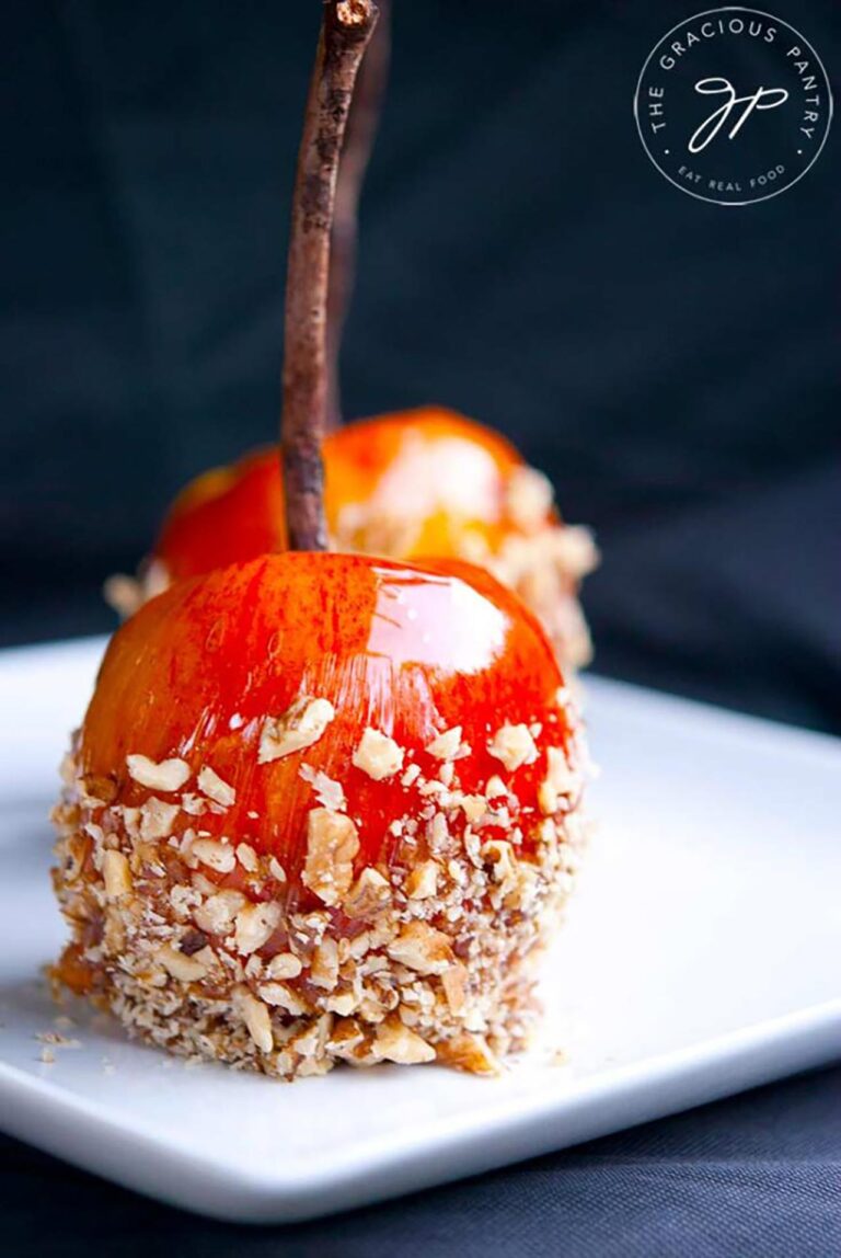 Front focus. Two candied apples coated in chopped walnuts sitting on a white platter.