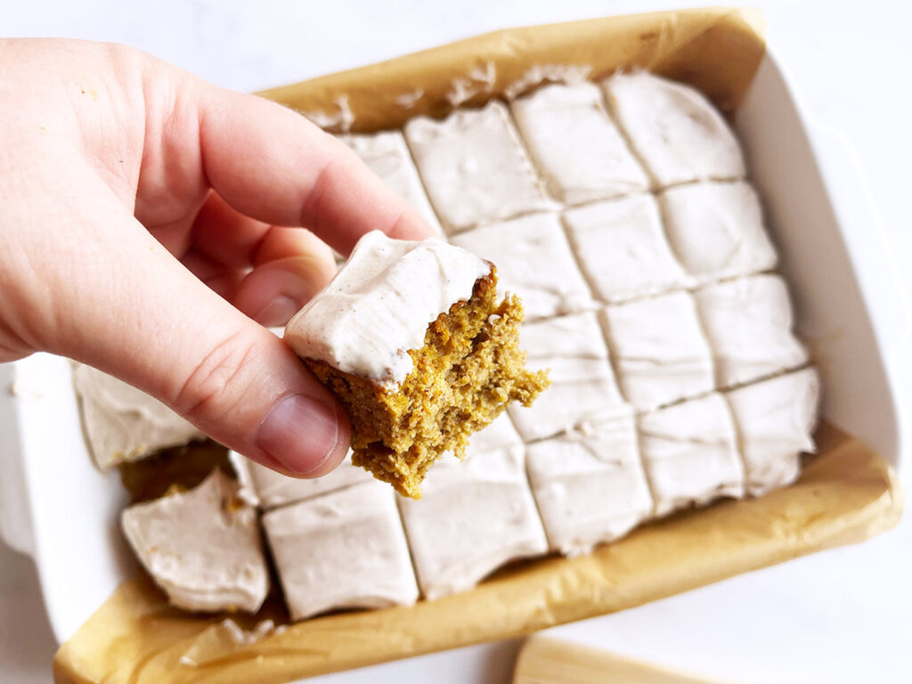 A hand holds a pumpkin bar with a bite taken from it.