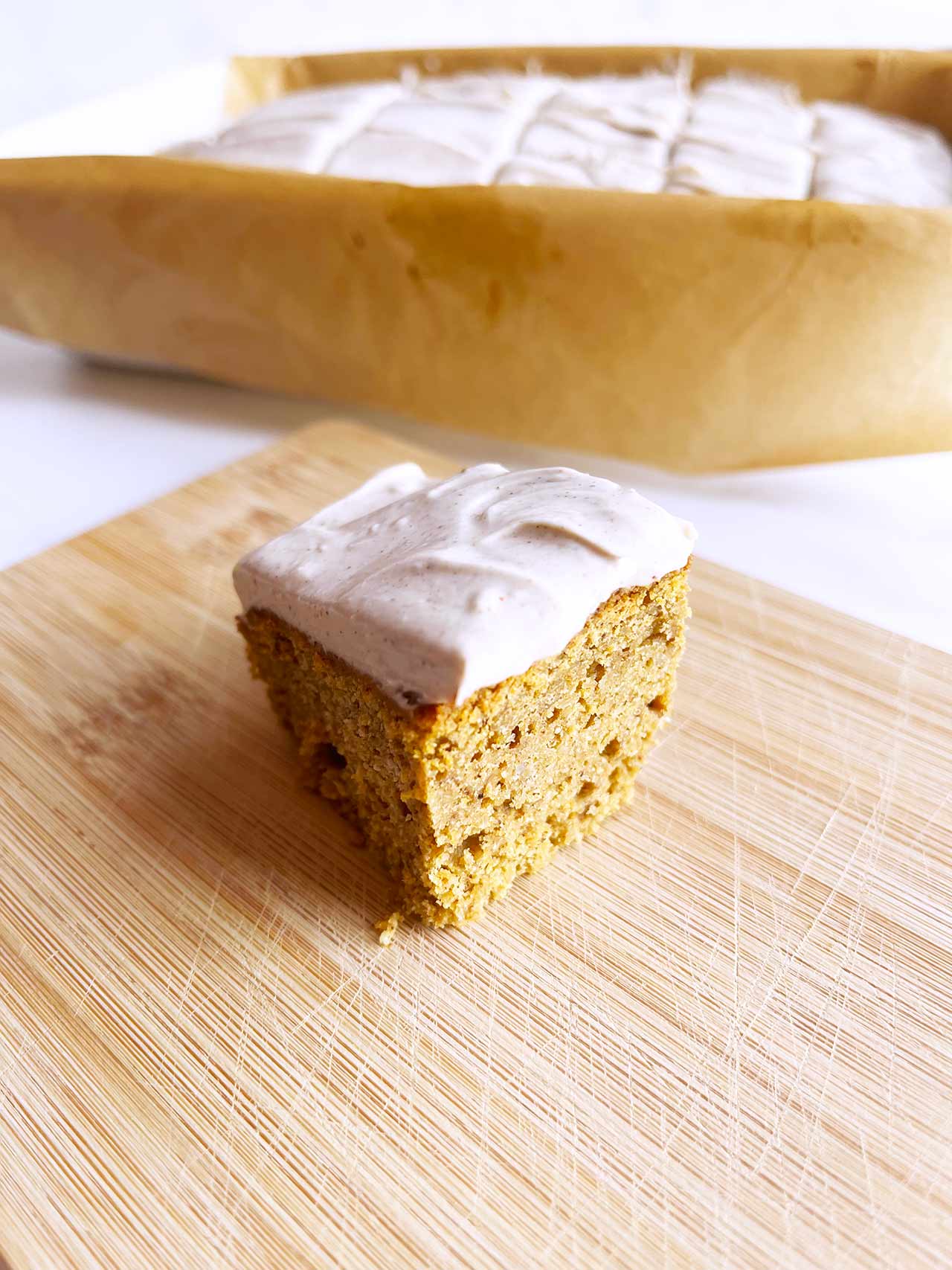 A pumpkin bar sits on a wood surface in front of the casserole dish it came from.