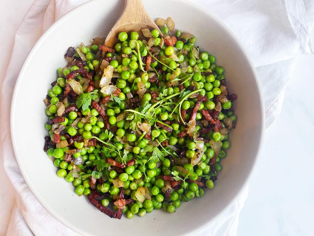 Overhead focus. A white bowl filled with Pea Salad.