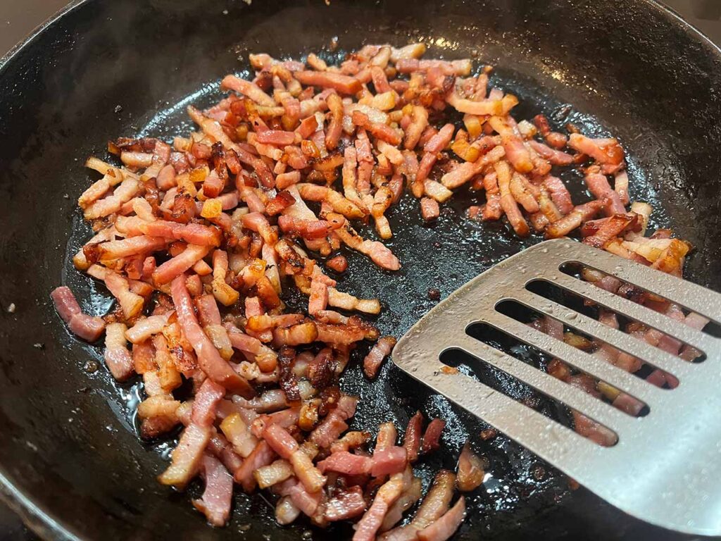 Chopped bacon cooking in a skillet.