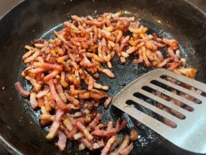 Chopped bacon cooking in a skillet.