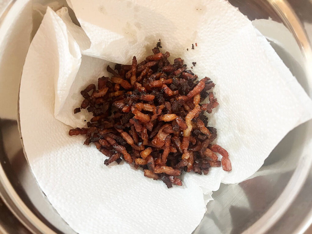 Cooked bacon pieces in a paper towel-lined bowl.