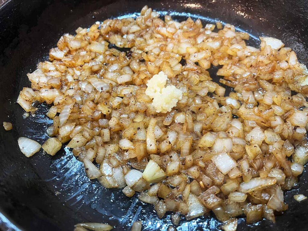 Pressed garlic added to cooked onions in a skillet.
