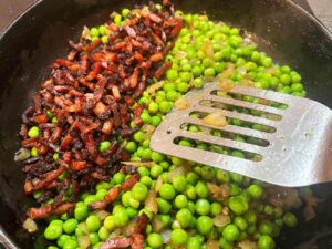 Adding the cooked bacon to the skillet.